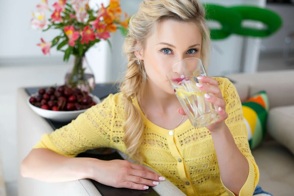 Woman in yellow shirt drinking a glass of water